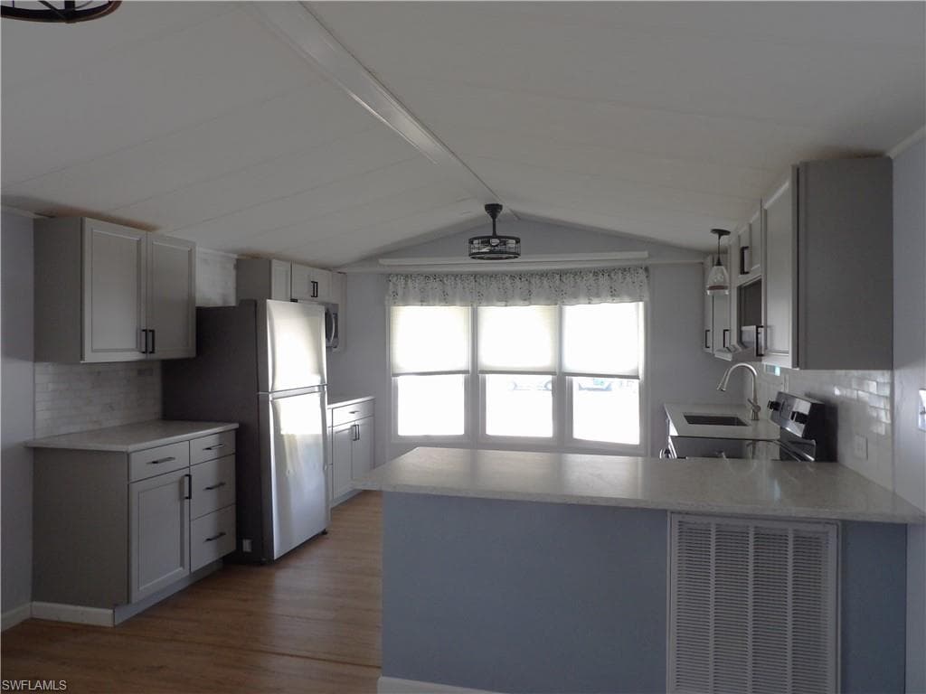 Kitchen featuring decorative backsplash, a peninsula, stainless steel appliances, gray cabinetry, and dark wood finished floors