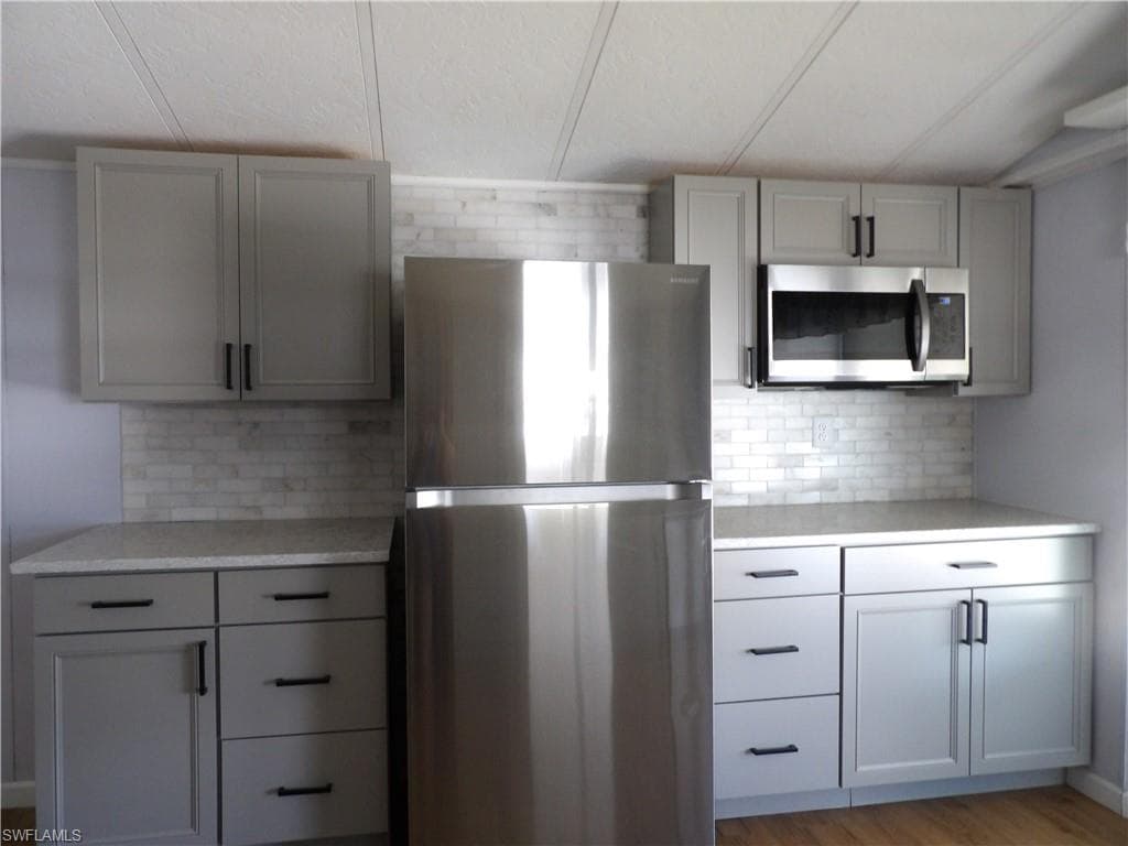 Kitchen with stainless steel appliances, tasteful backsplash, gray cabinetry, and light stone countertops
