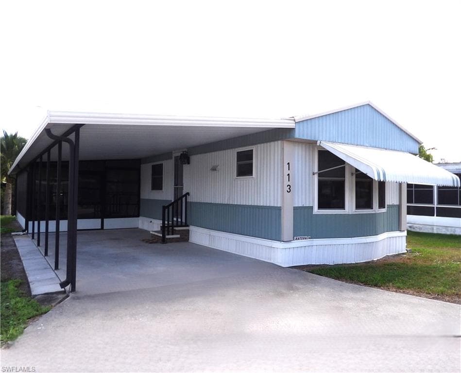 View of front of property featuring a sunroom, an attached carport, driveway, and a patio area