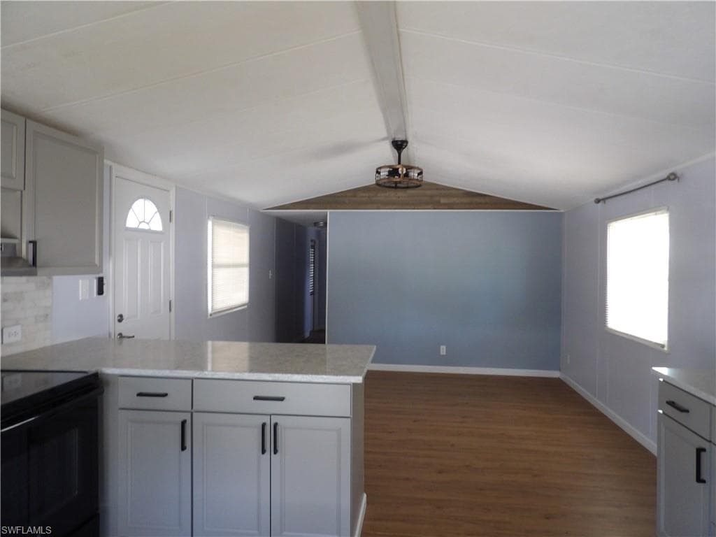Kitchen featuring a peninsula, laminated flooring, beam ceiling, black range with electric cooktop, and light stone counters