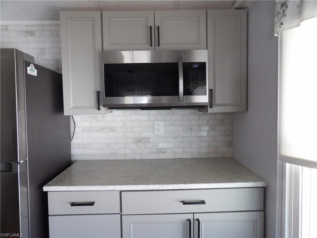 Kitchen with stainless steel appliances, gray cabinetry, and tasteful backsplash