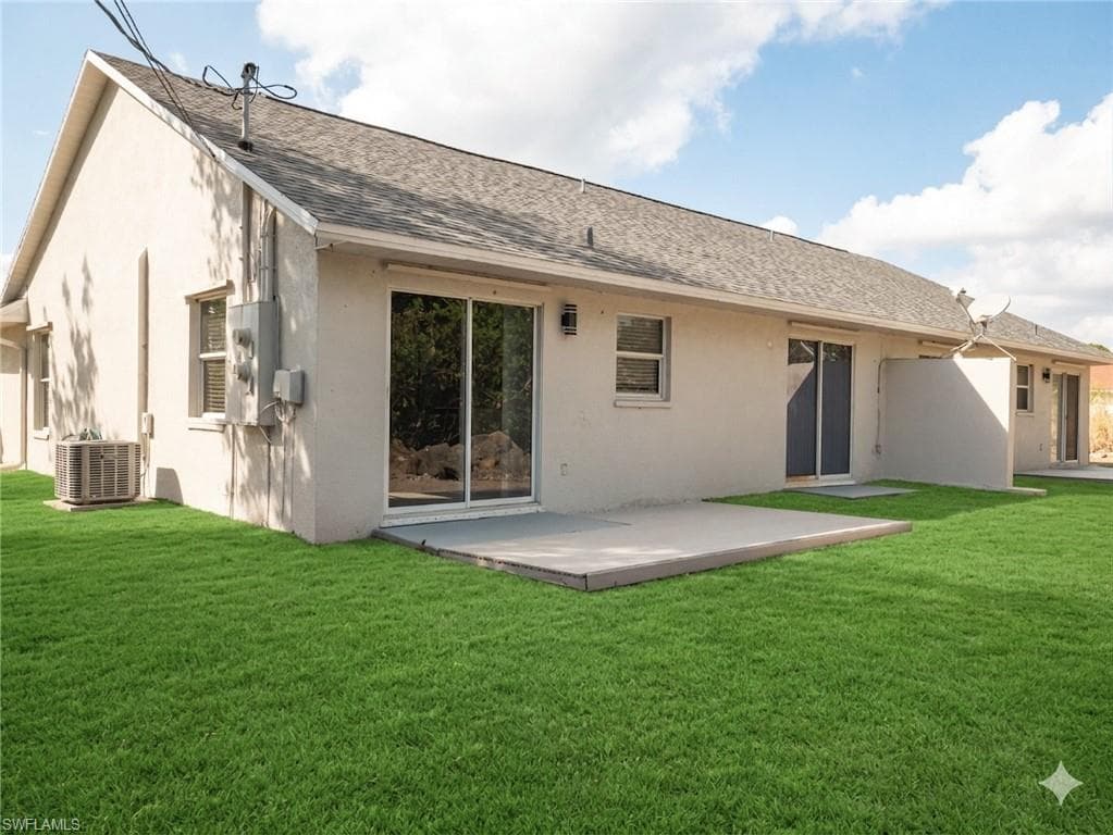 Rear view of property featuring roof with shingles, a yard, stucco siding, and a patio