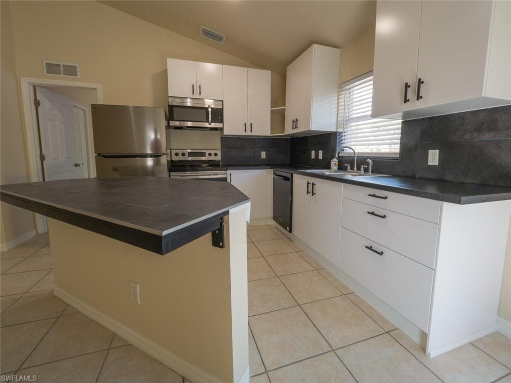 Kitchen with sink, a center island, lofted ceiling, white cabinets, and appliances with stainless steel finishes