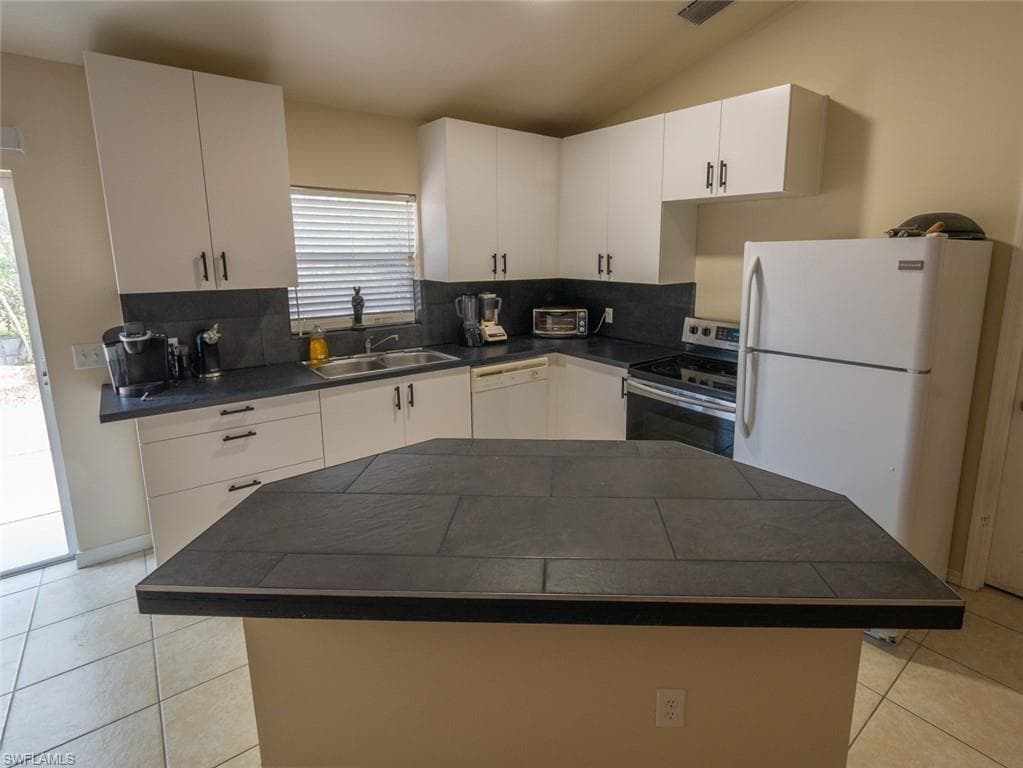 Kitchen with decorative backsplash, white appliances, vaulted ceiling, sink, and white cabinets