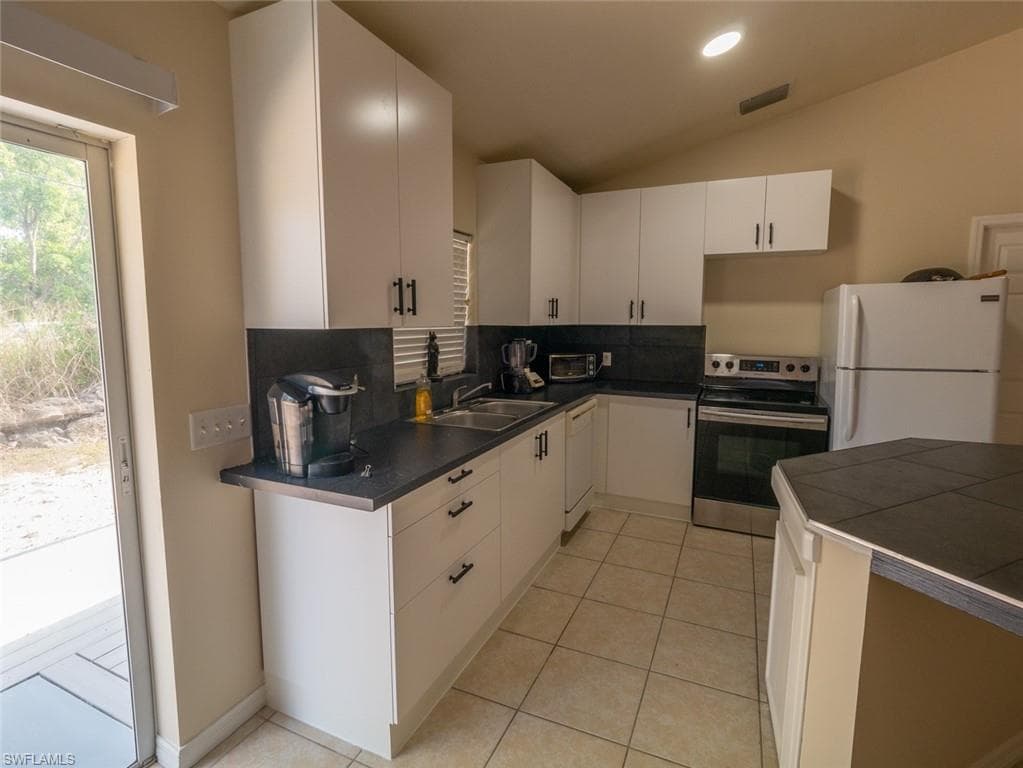 Kitchen featuring vaulted ceiling, light tile patterned floors, white cabinets, and white appliances