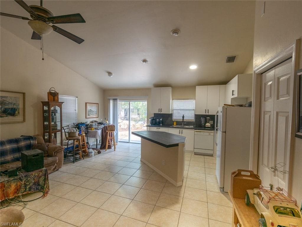 Kitchen with lofted ceiling, white appliances, sink, light tile patterned floors, and white cabinetry