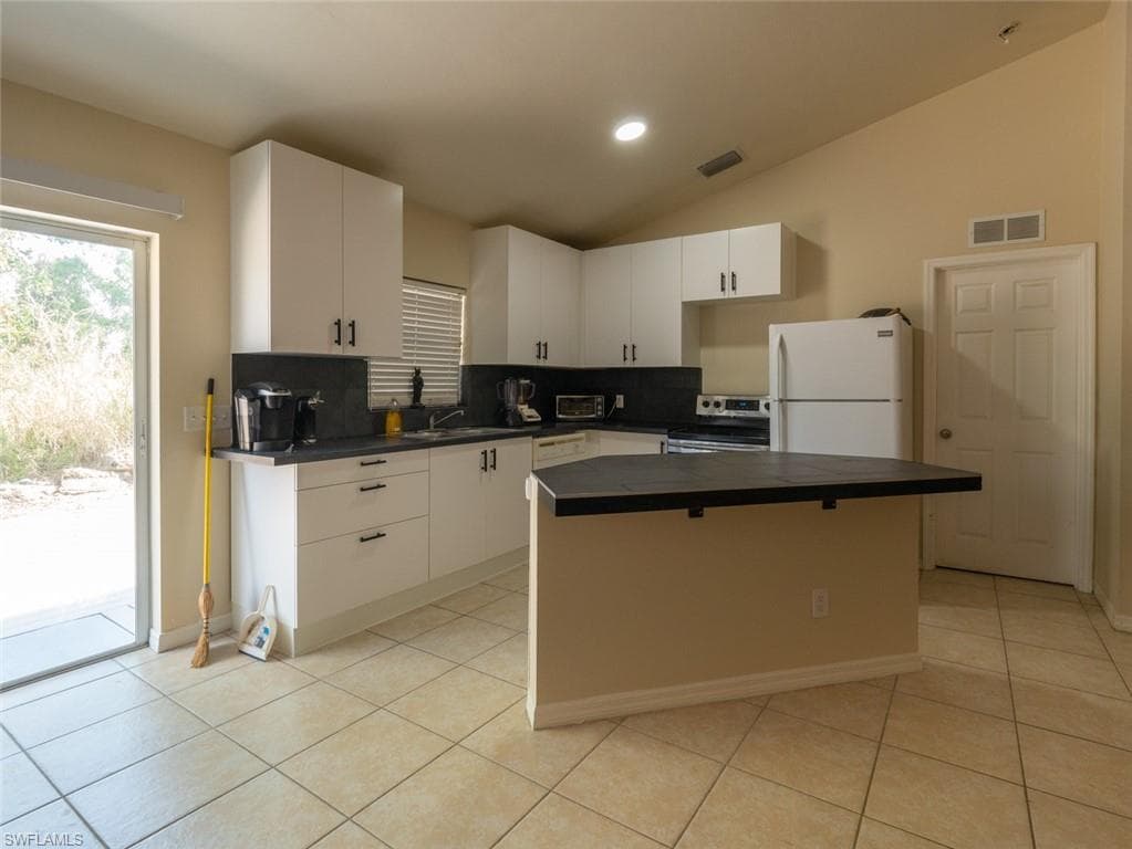 Kitchen featuring a center island, white fridge, lofted ceiling, and backsplash