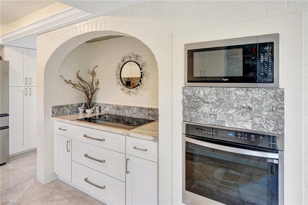 Kitchen with white cabinetry, light stone countertops, appliances with stainless steel finishes, and backsplash