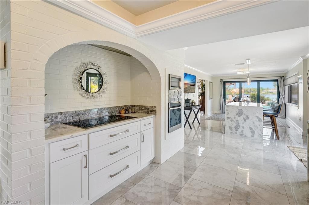 Kitchen featuring white cabinets, marble finish floor, ornamental molding, stainless steel oven, and black electric stovetop