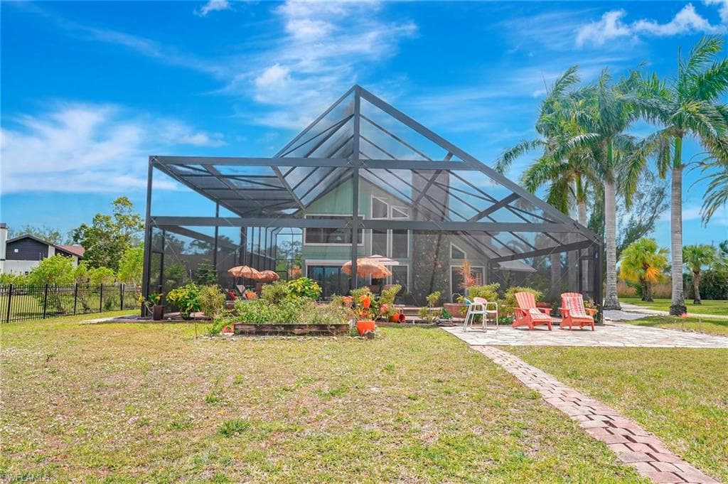 Back of property with glass enclosure, fence, a lawn, and a patio area