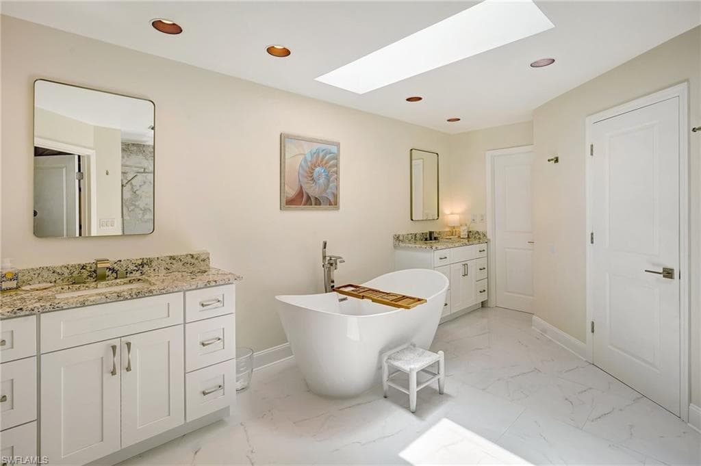 Bathroom featuring recessed lighting, a soaking tub, marble finish floor, a sink, and a skylight