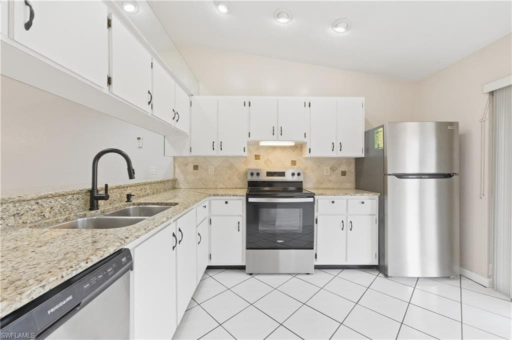 Kitchen with stainless steel appliances, light stone countertops, backsplash, lofted ceiling, and white cabinets