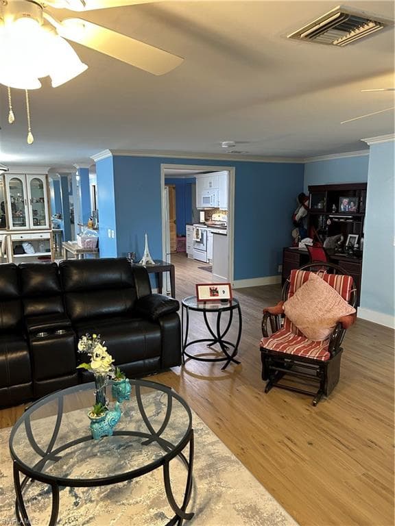 Living room with a ceiling fan, light wood-style flooring, and crown molding