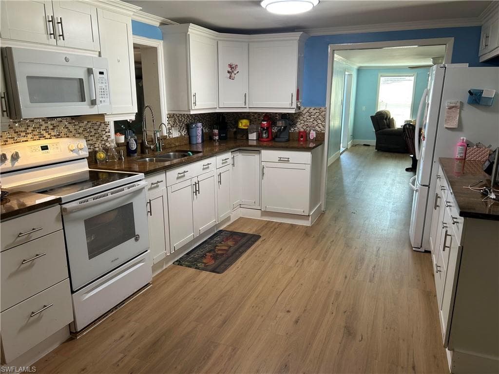 Kitchen featuring white appliances, white cabinets, light wood-style flooring, ornamental molding, and dark stone countertops