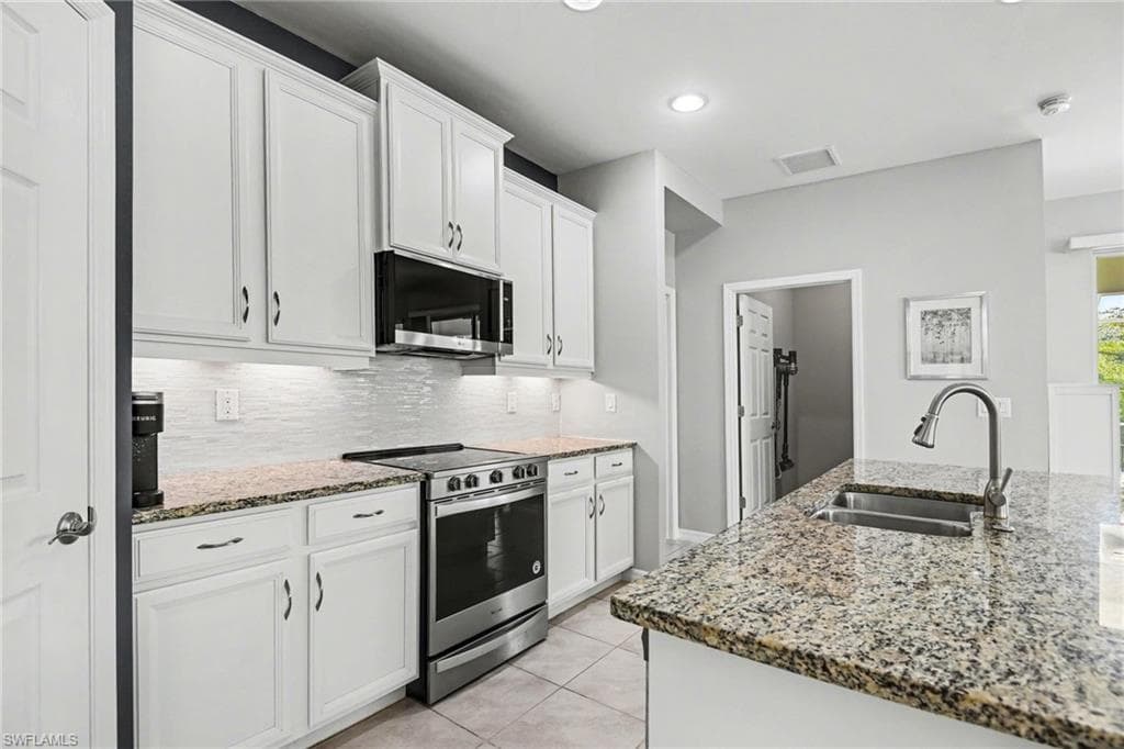 Kitchen with stainless steel appliances, white cabinetry, light stone counters, light tile patterned floors, and decorative backsplash