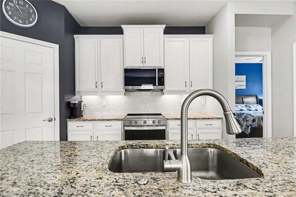 Kitchen with white cabinets, stainless steel appliances, backsplash, and light stone countertops