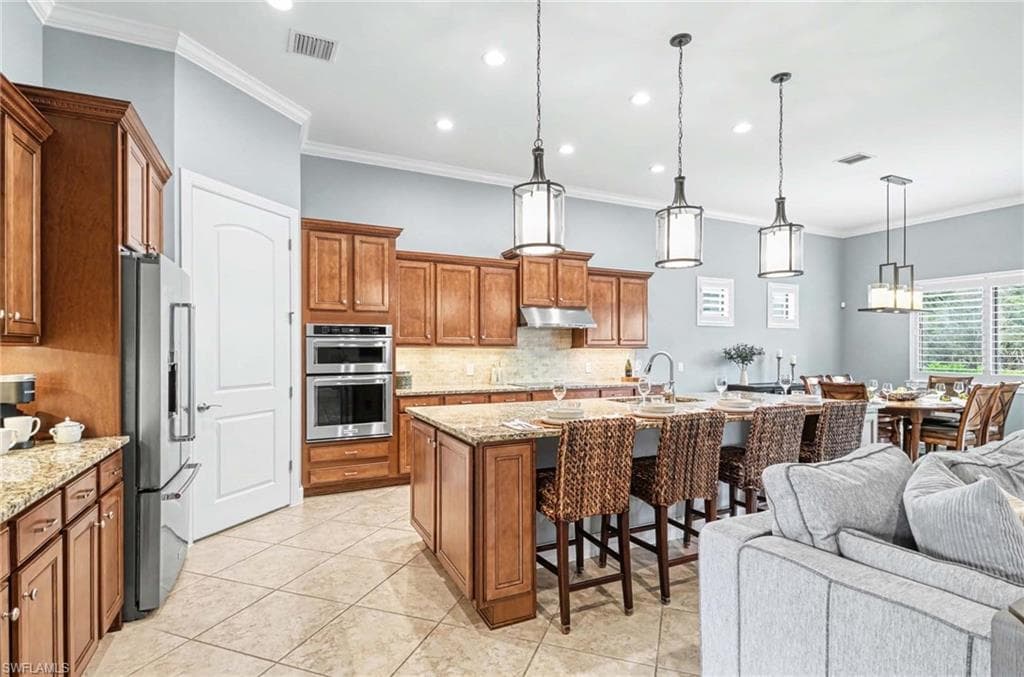 Kitchen with wood finish cabinets, a kitchen breakfast bar, a kitchen island with sink, light stone counters, and stainless steel appliances