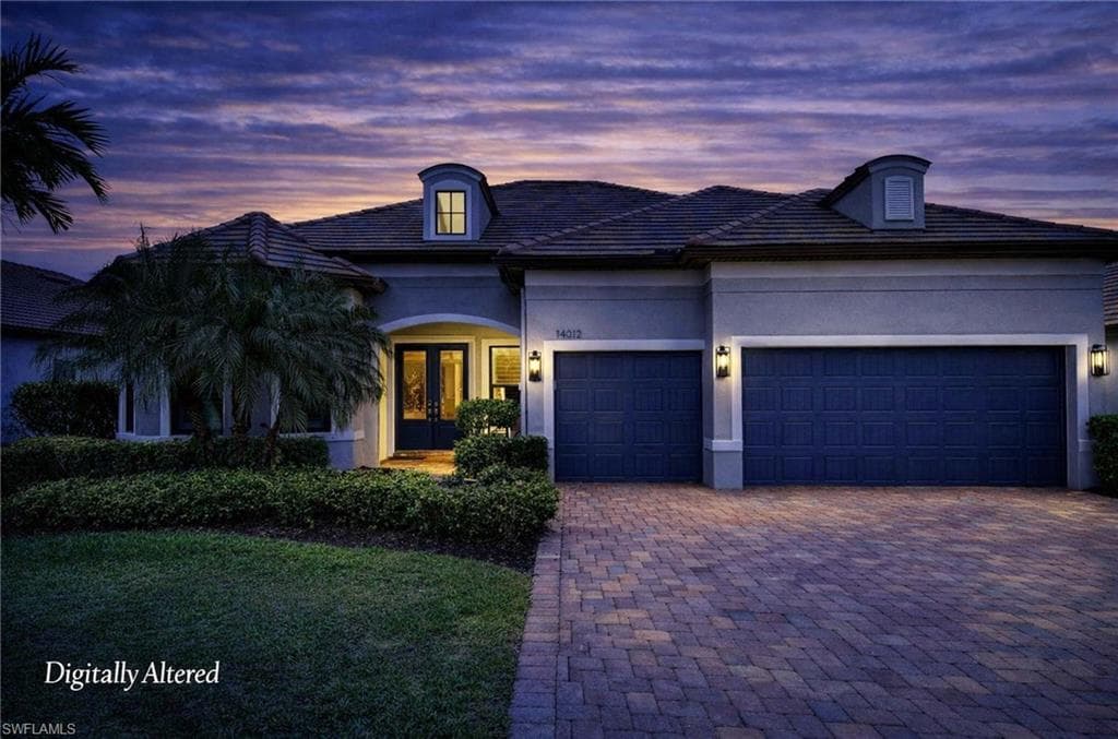 Stucco exterior with a tiled roof, paver driveway, and a two-car garage