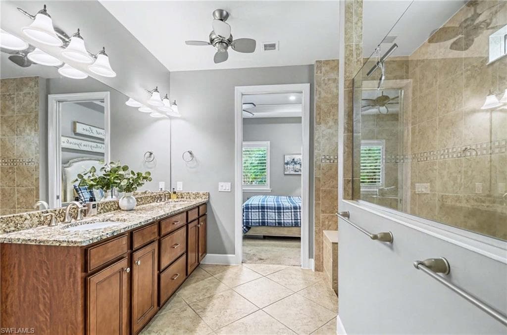 Ensuite bathroom featuring double vanity, walk in shower, light tile patterned flooring, and a ceiling fan