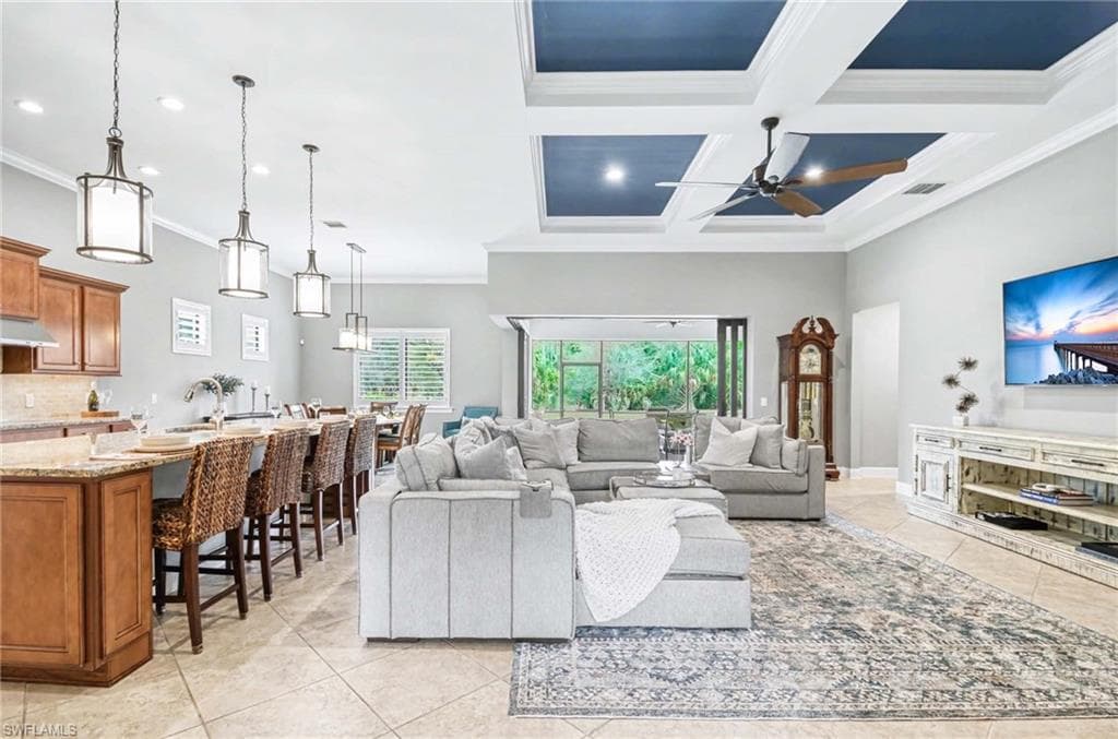Living room featuring coffered ceiling, crown molding, light tile patterned flooring, and a ceiling fan