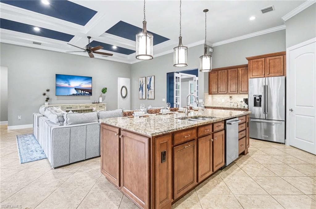 Kitchen featuring wood finish cabinetry, a center island with sink, stainless steel appliances, light stone counters, and open floor plan