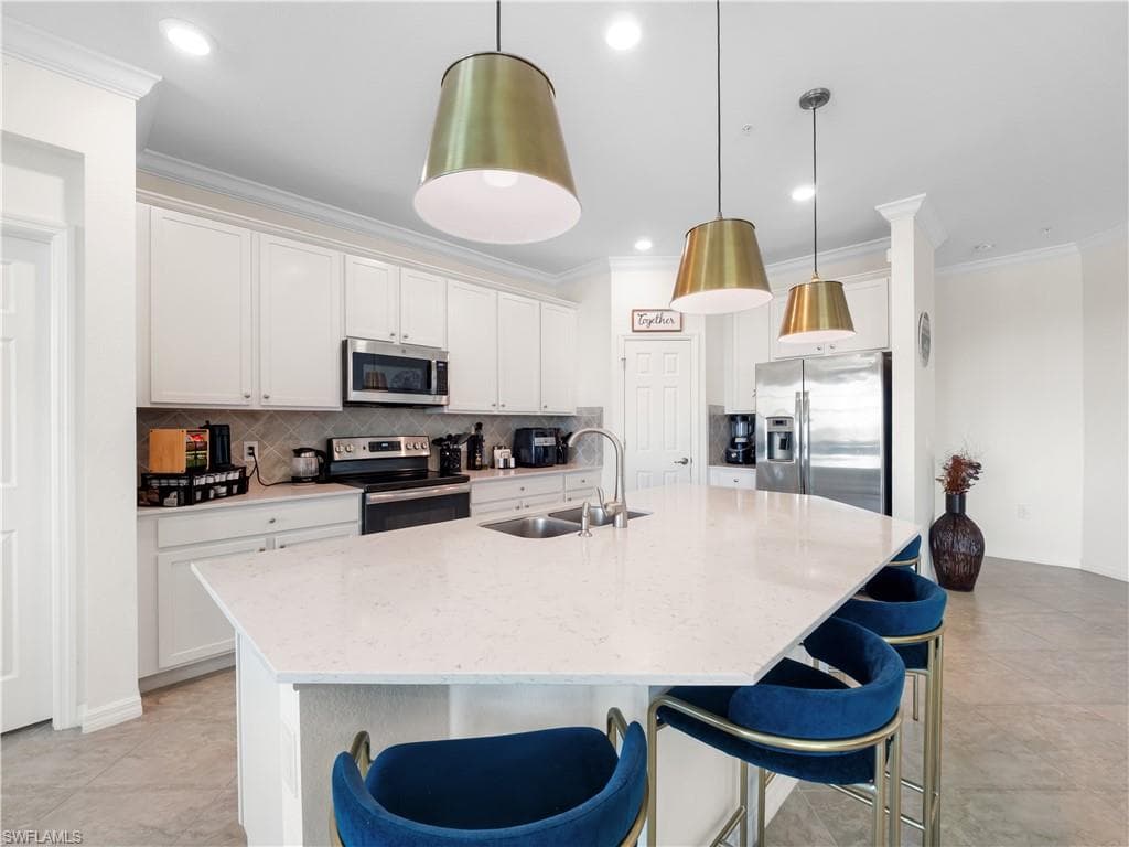Kitchen with a breakfast bar area, stainless steel appliances, crown molding, an island with sink, and decorative backsplash