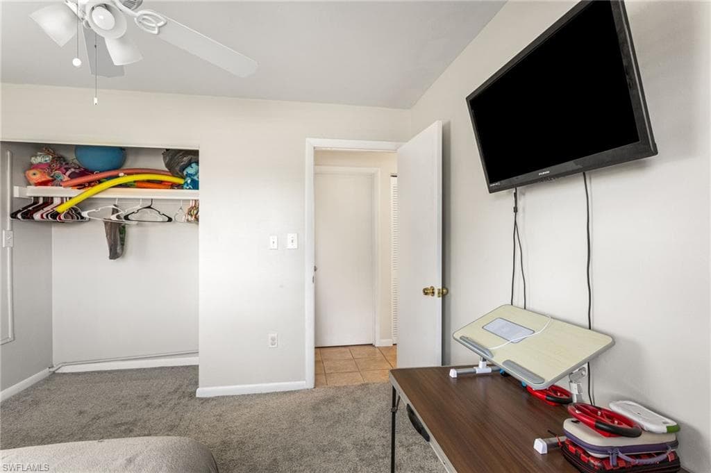 Bedroom with light colored carpet, ceiling fan, and light tile patterned floors