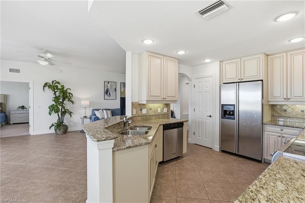 Kitchen featuring cream cabinetry, stainless steel appliances, light stone counters, a ceiling fan, and light tile patterned flooring