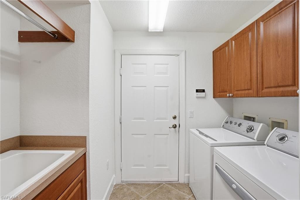 Laundry area featuring cabinet space, separate washer and dryer, light tile patterned floors, and a textured ceiling