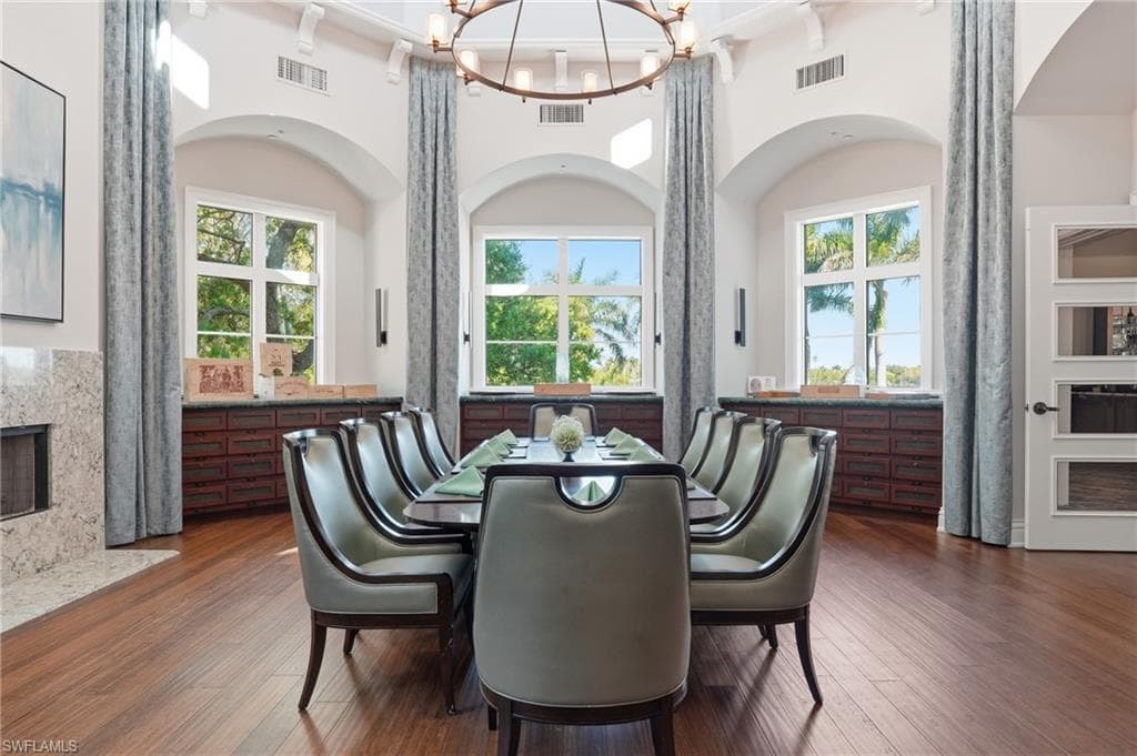 Dining room with suspended lighting, a fireplace, a high ceiling, dark wood-style floors, and healthy amount of natural light