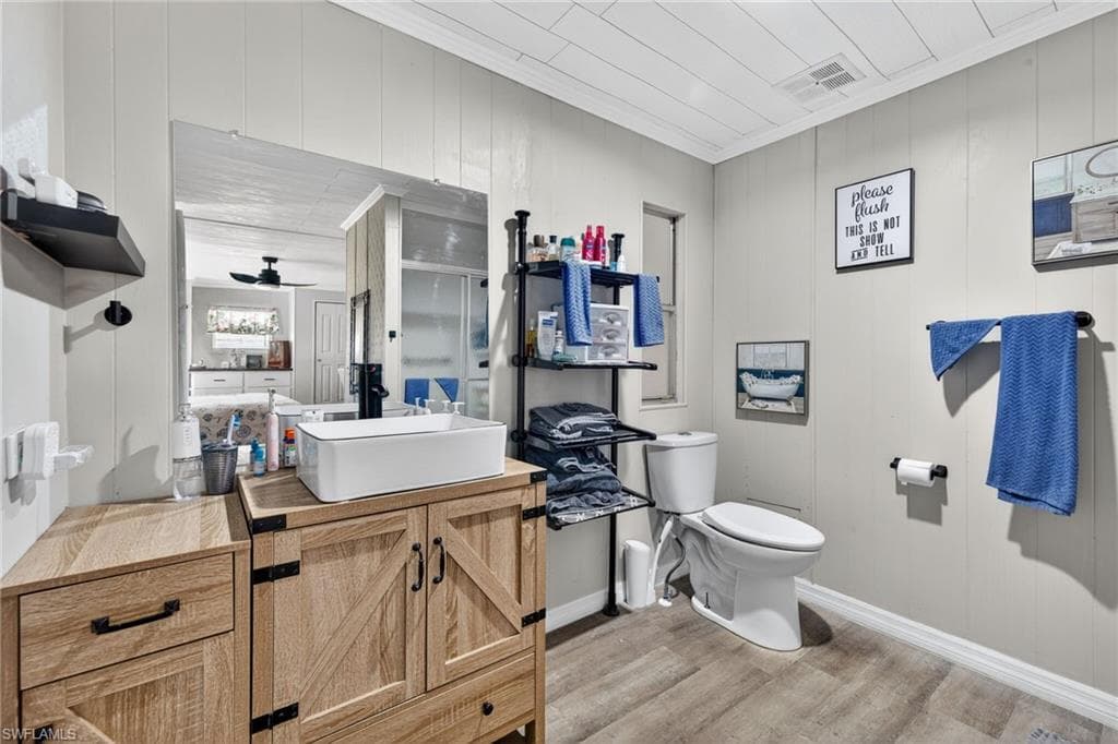 Full bath featuring wooden walls, vanity, light wood finished floors, crown molding, and ceiling fan
