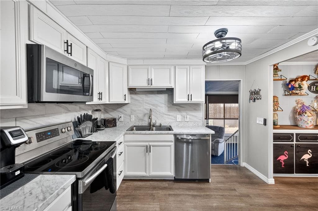 Kitchen with stainless steel appliances, light countertops, white cabinets, dark wood-style floors, and ornamental molding