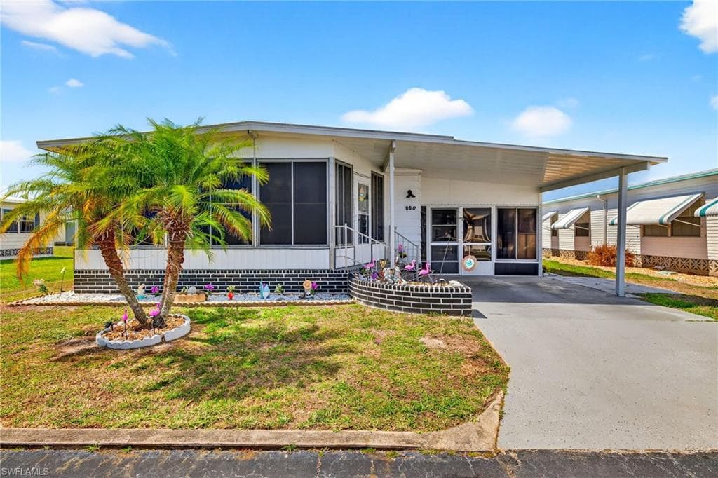 Manufactured / mobile home featuring a sunroom, an attached carport, a front lawn, and driveway