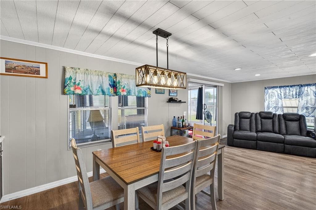 Dining room with dark wood finished floors, wood walls, and crown molding