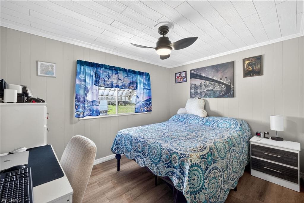 Bedroom with wood finished floors, an office area, ceiling fan, and wood walls