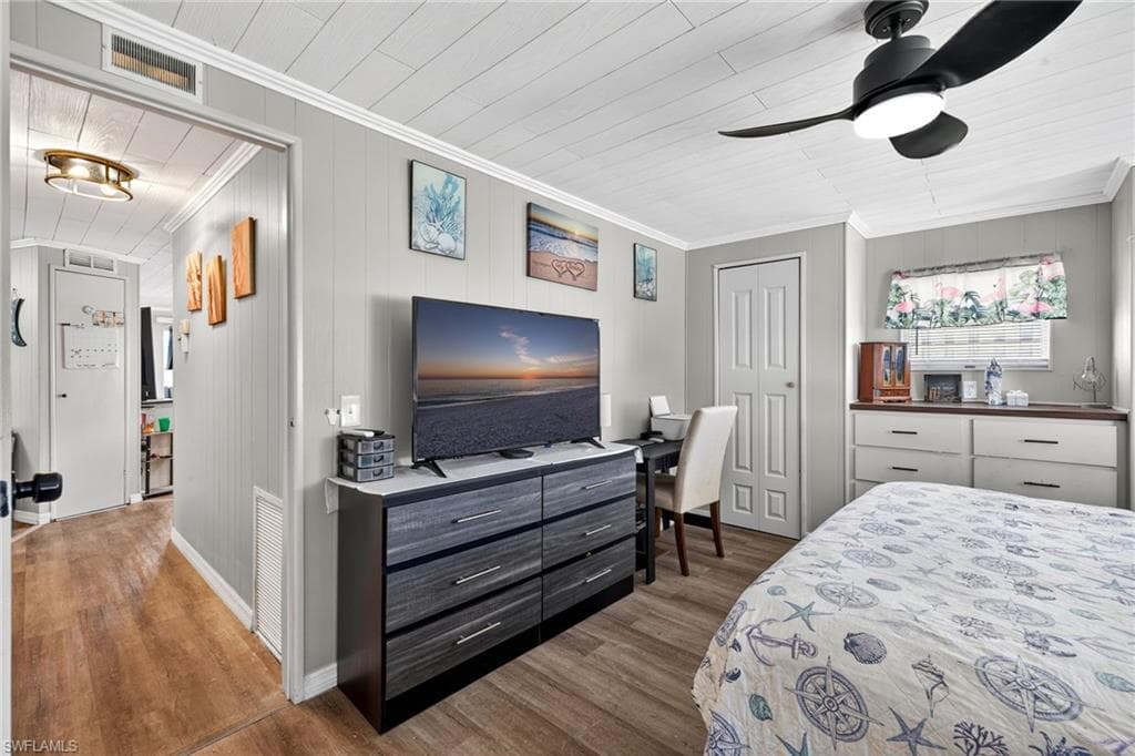 Bedroom featuring wood walls, wood finished floors, a closet, a ceiling fan, and crown molding