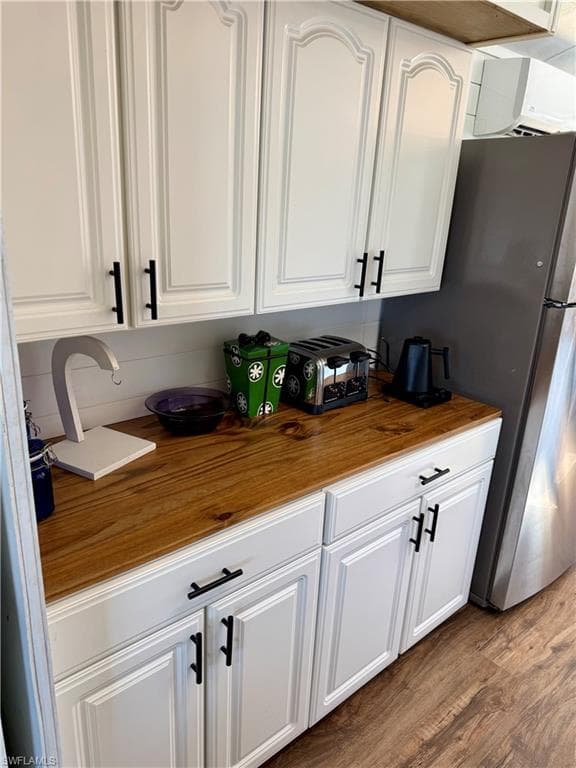 Kitchen view of white cabinets, wooden counters, dark wood-type flooring, and freestanding refrigerator