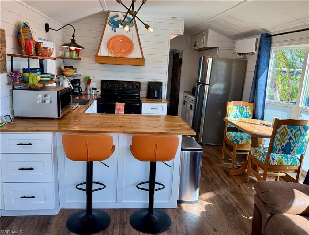 Kitchen featuring wood counters, black electric range, range hood, freestanding refrigerator, and dark wood finished floors