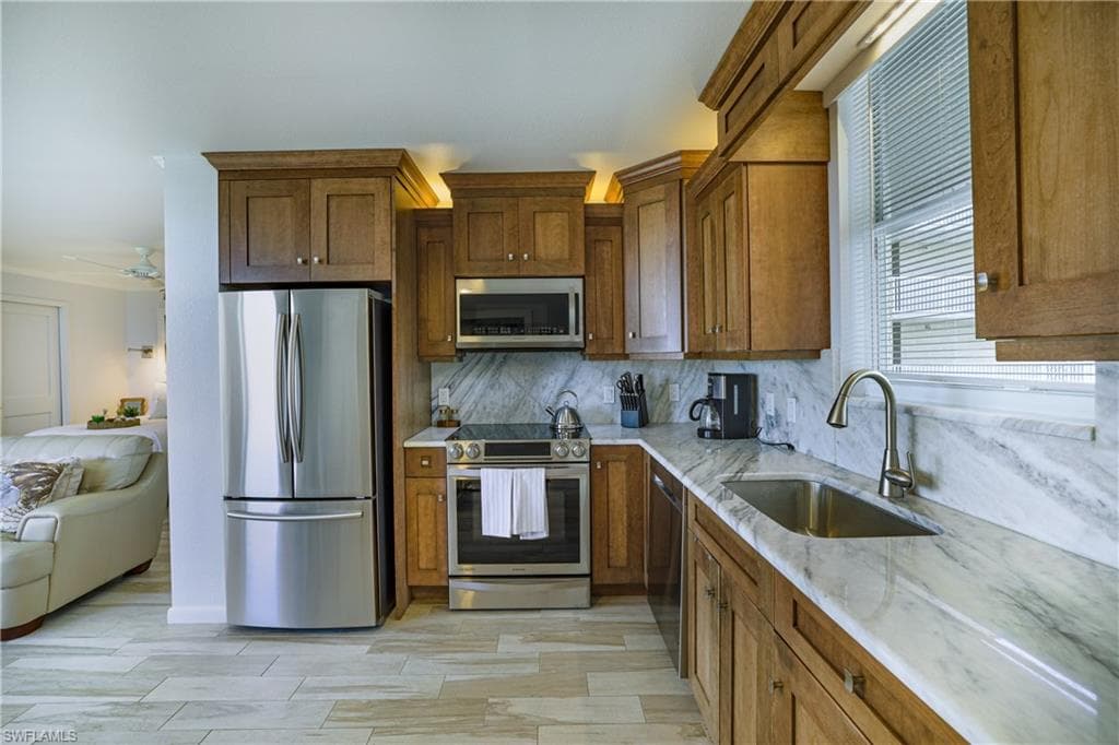 Kitchen featuring stainless steel appliances, light stone countertops, wood finish cabinetry, and ceiling fan