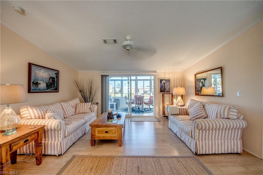 Living room with light wood finished floors, a ceiling fan, ornamental molding, and a textured ceiling