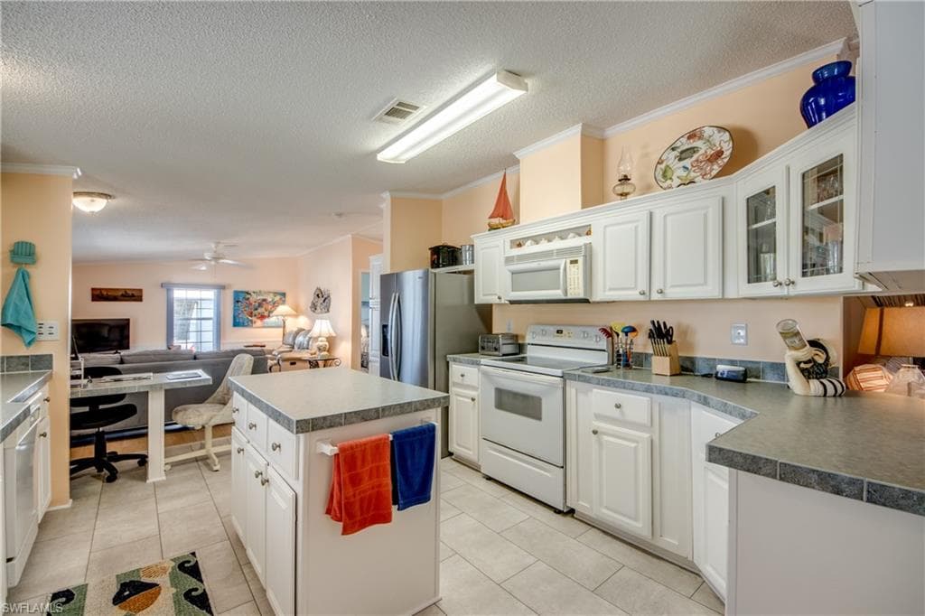 Kitchen with white appliances, open floor plan, white cabinets, crown molding, and a kitchen island