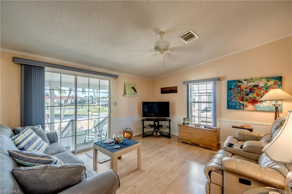 Living room with light wood-style flooring, crown molding, ceiling fan, and a wainscoted wall