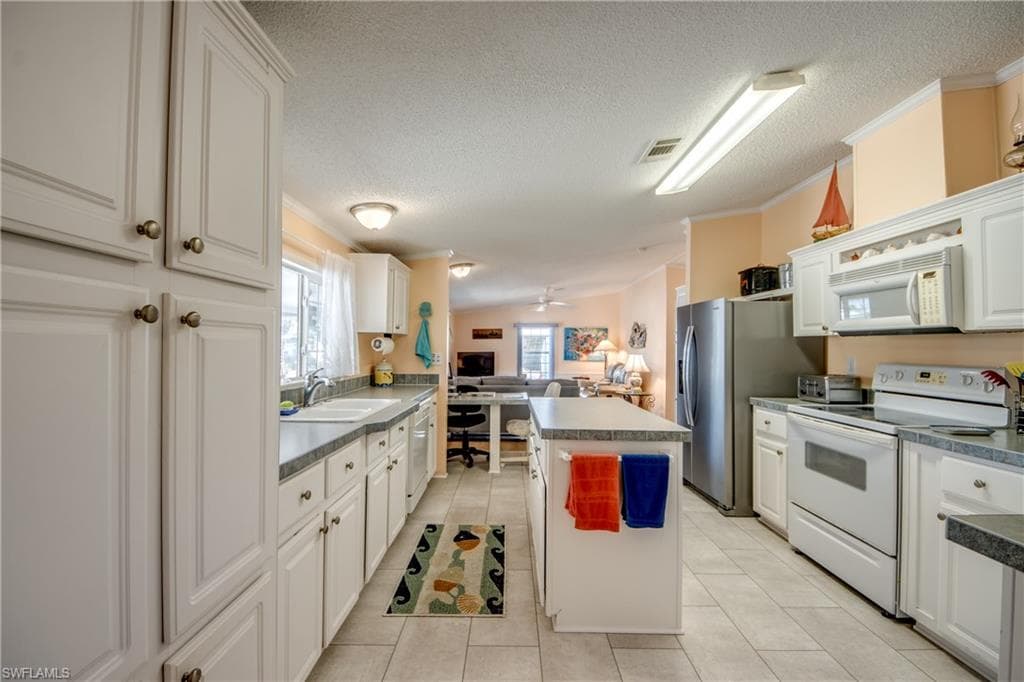 Kitchen featuring a center island, white appliances, crown molding, white cabinetry, and light tile patterned floors