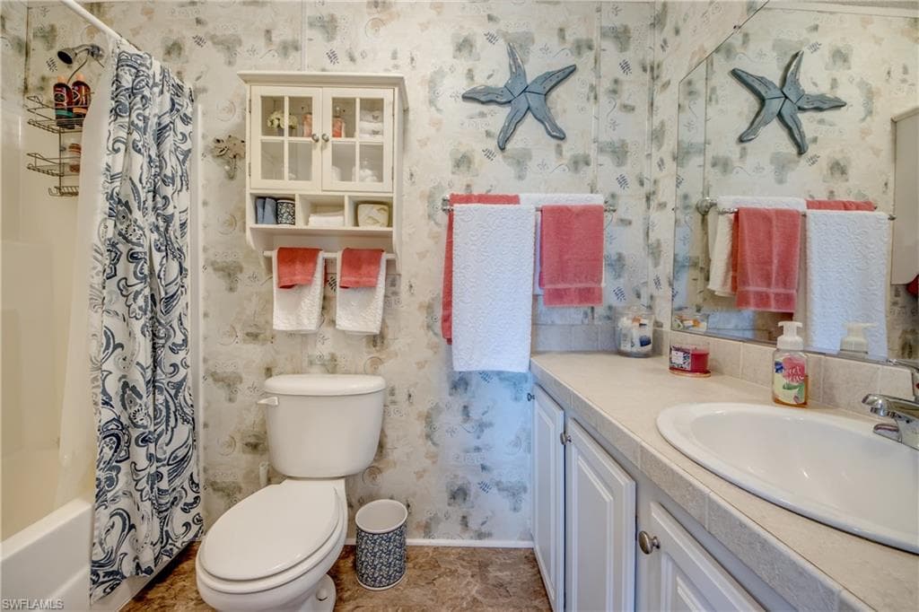 Bathroom with wallpapered walls, vanity, and shower / bath combo