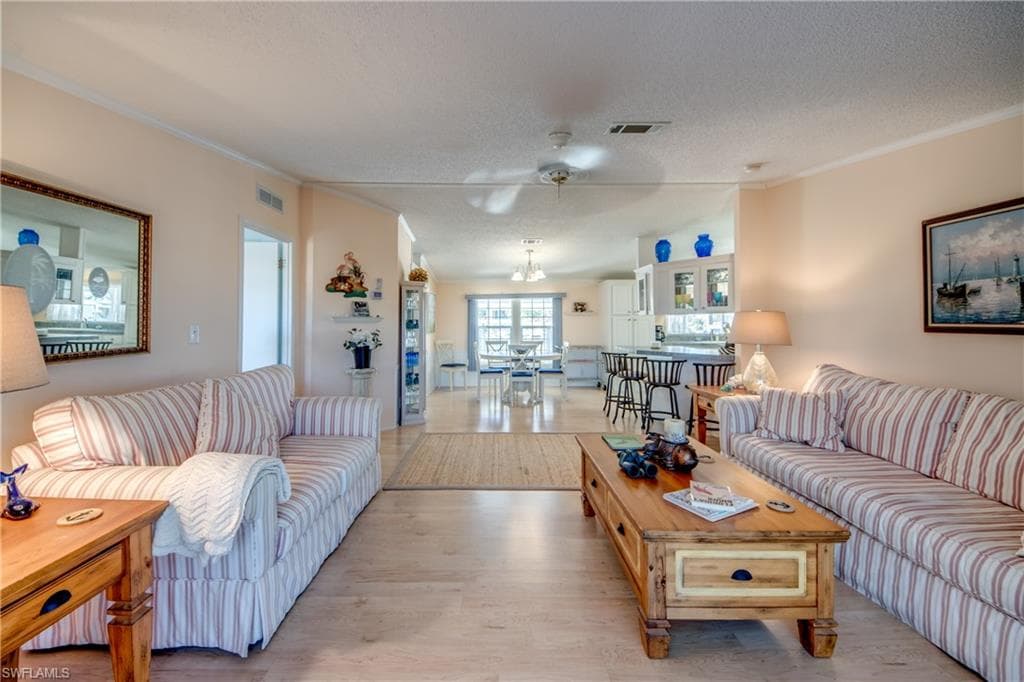 Living area with ornamental molding, light wood finished floors, a textured ceiling, and ceiling fan