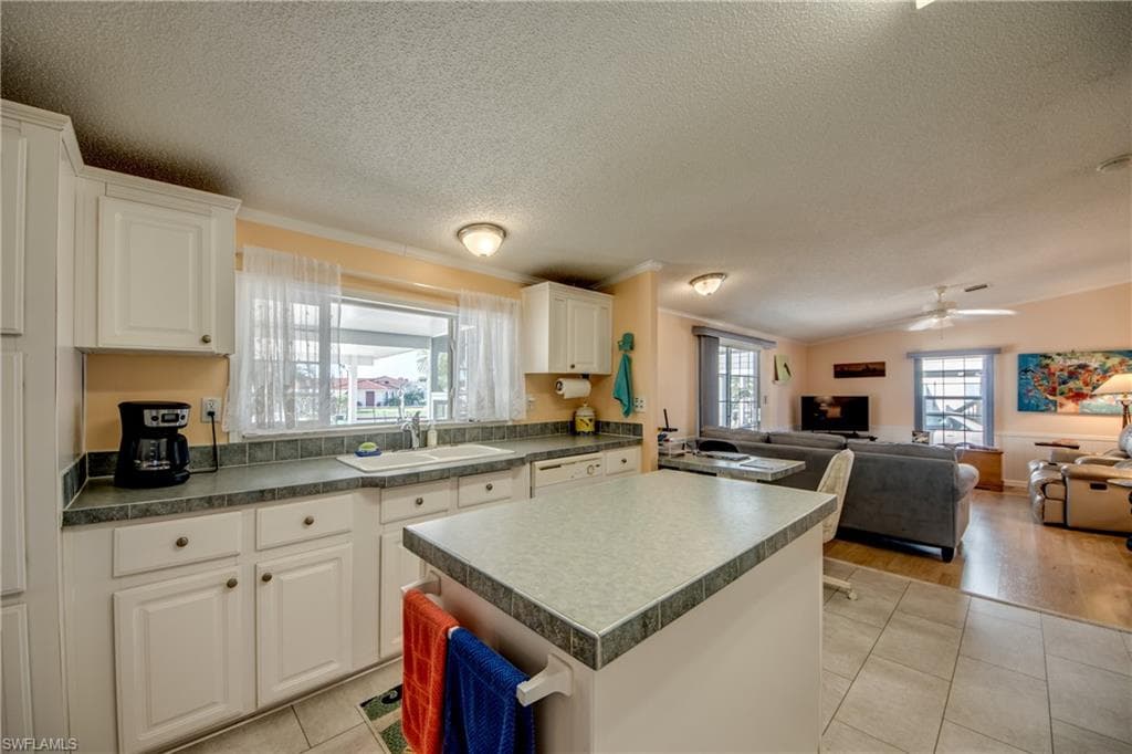 Kitchen featuring open floor plan, white cabinetry, a center island, dark countertops, and ornamental molding