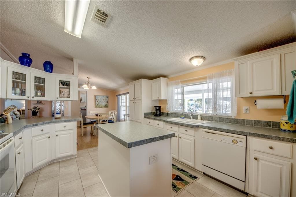 Kitchen featuring white cabinets, white appliances, a kitchen island, and light tile patterned floors
