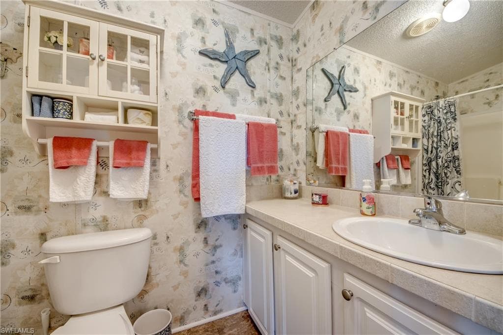 Bathroom with vanity, a shower with curtain, wallpapered walls, and a textured ceiling