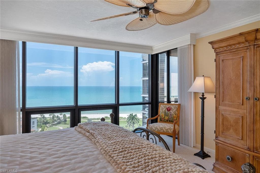 Carpeted bedroom with multiple windows, view of water and beach, expansive windows, crown molding, and ceiling fan