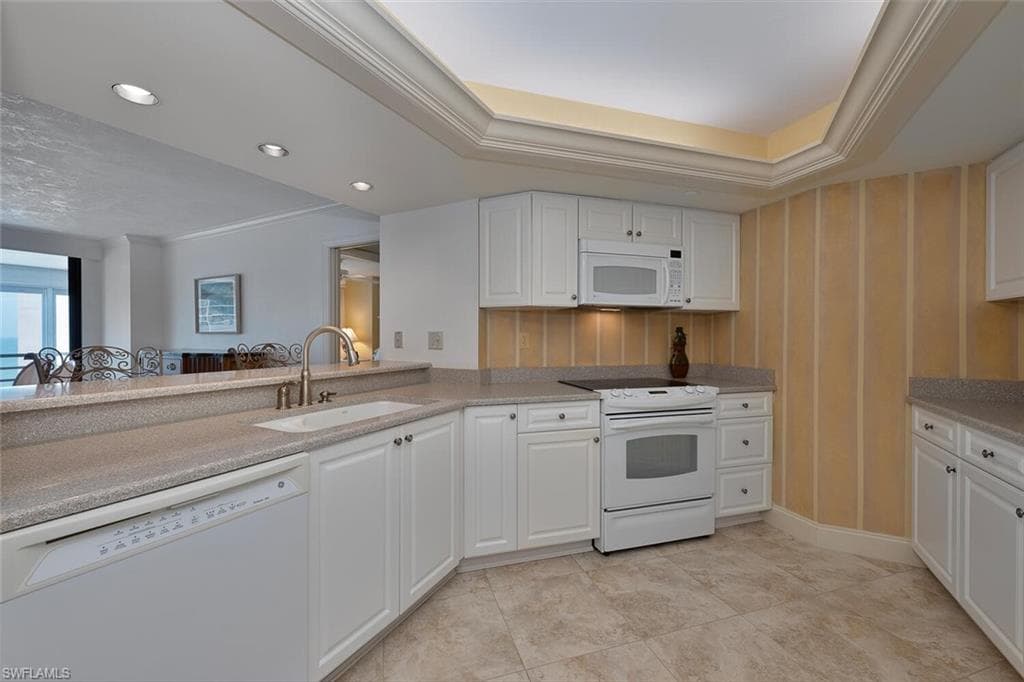 Kitchen with crown molding, white appliances, white cabinets, recessed lighting, and light stone counters